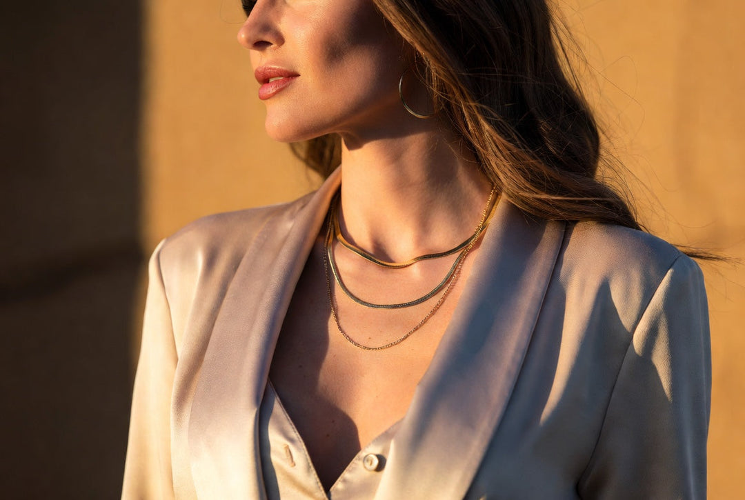 Elegant woman with layered gold necklaces transitioning from workwear to evening style during golden hour.