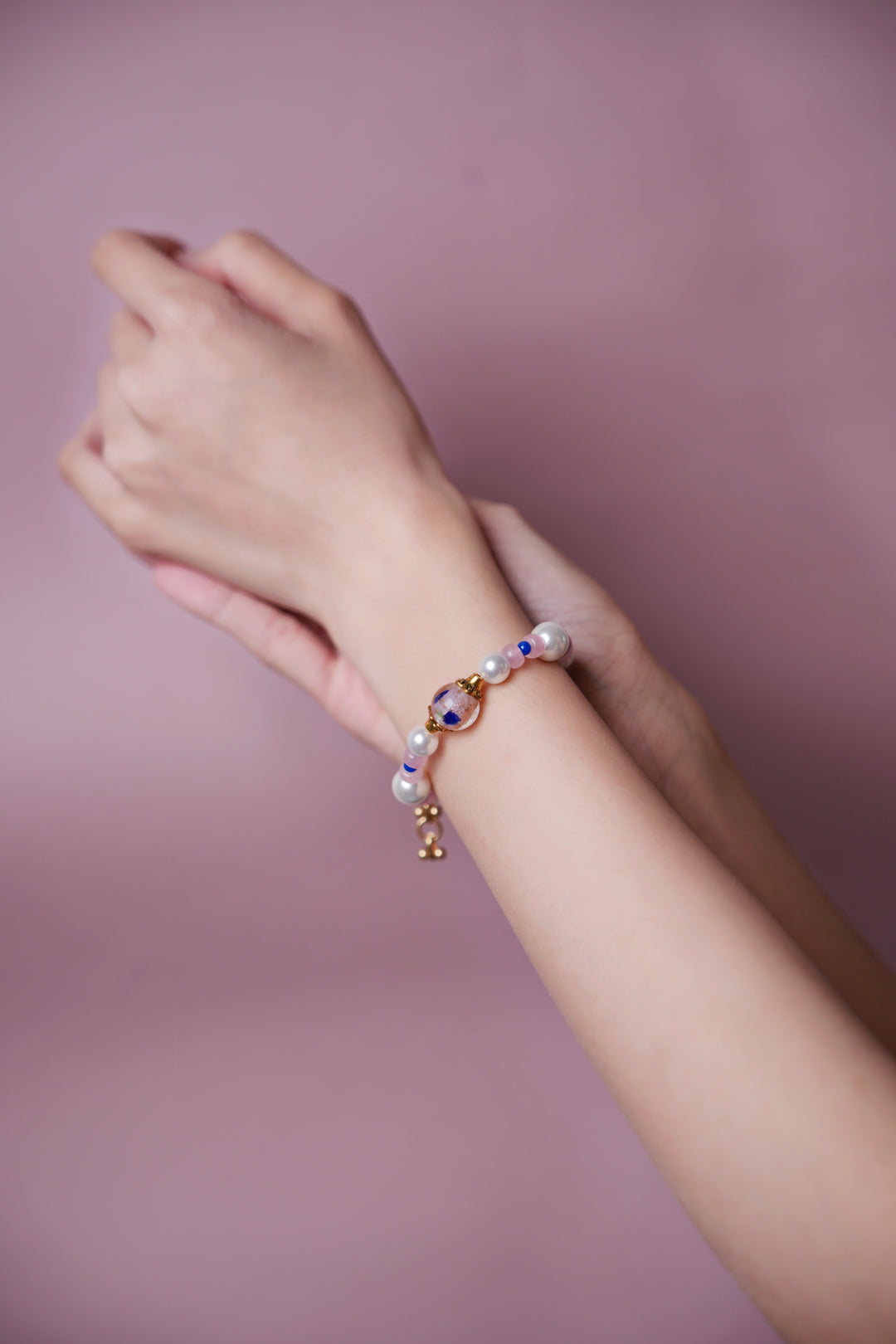 A hand wearing a Artisanal Oriental style pearl and pink gemstone bracelet with a hand-painted floral glass bead, vintage Eastern aesthetic boutique jewelry.