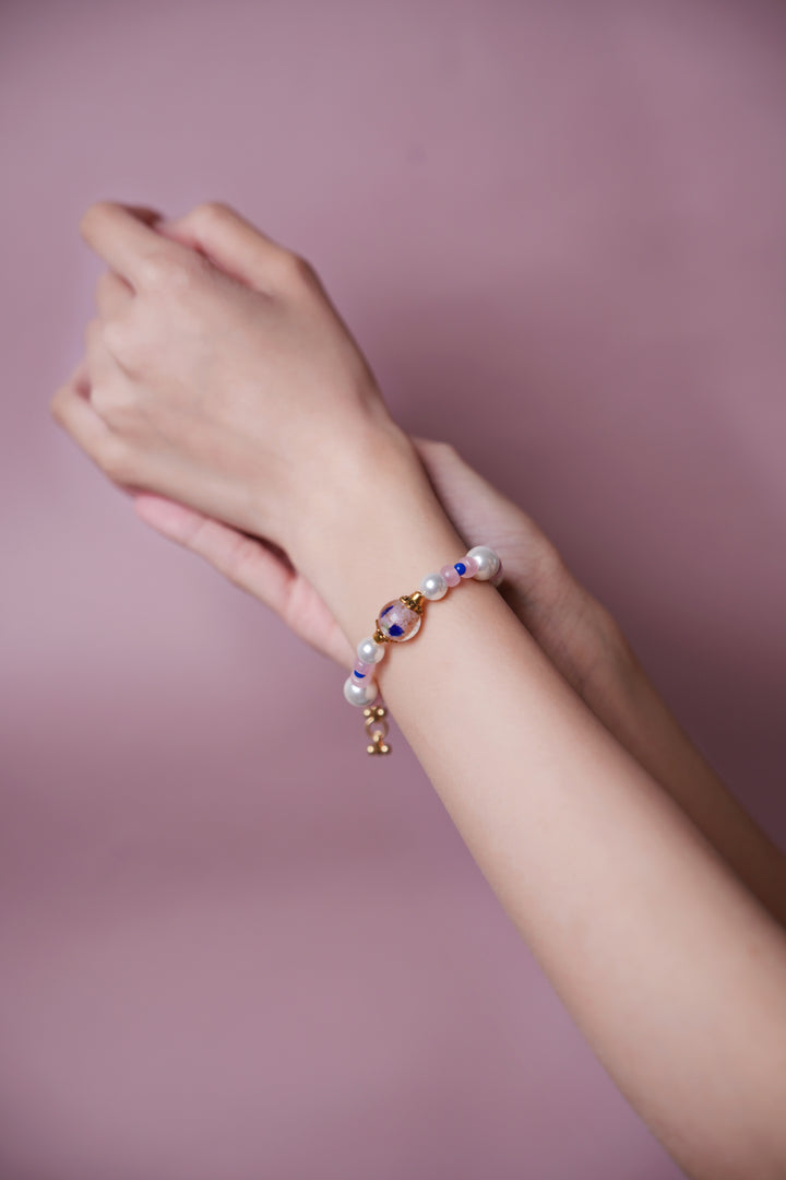 A hand wearing a Artisanal Oriental style pearl and pink gemstone bracelet with a hand-painted floral glass bead, vintage Eastern aesthetic boutique jewelry.
