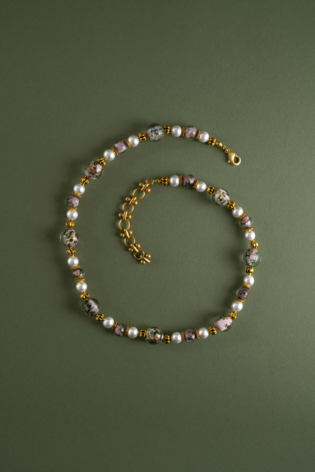 Artisanal Oriental style Liuli glass flower bead necklace with freshwater pearls and retro gold details, vintage Eastern aesthetic statement jewelry on a green background.