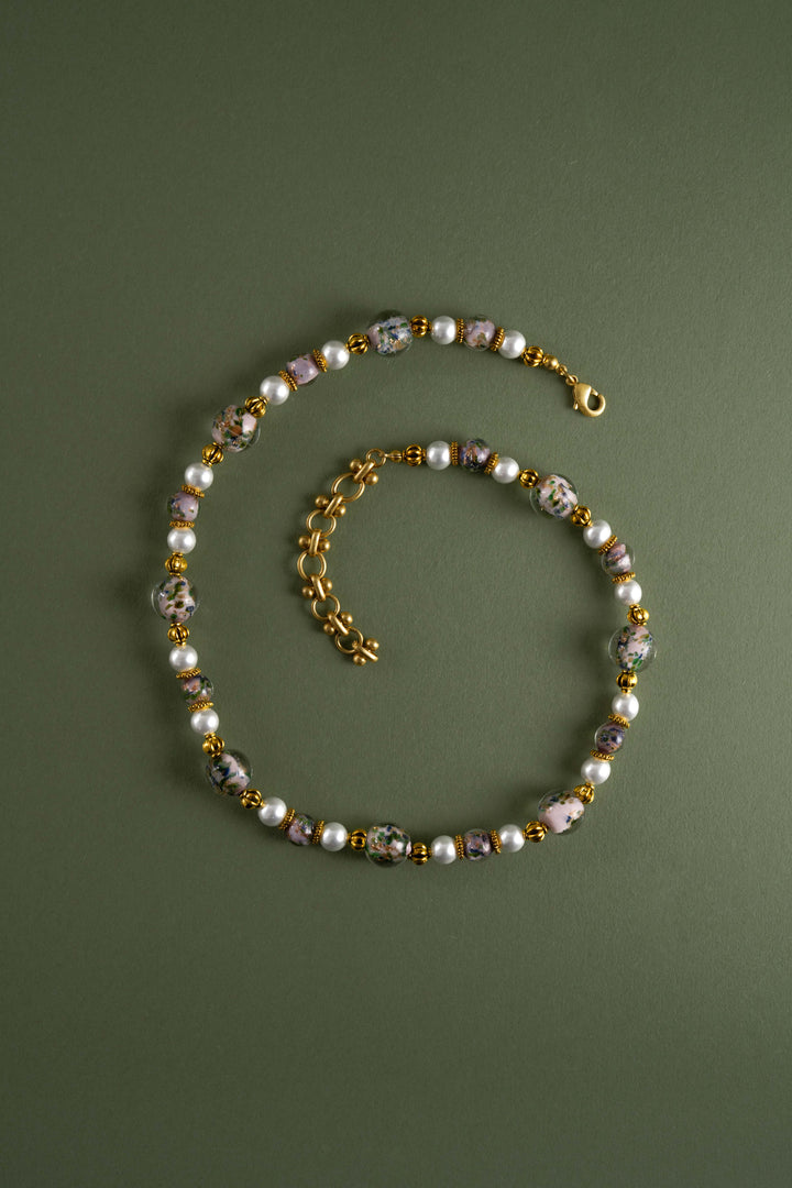 Artisanal Oriental style Liuli glass flower bead necklace with freshwater pearls and retro gold details, vintage Eastern aesthetic statement jewelry on a green background.