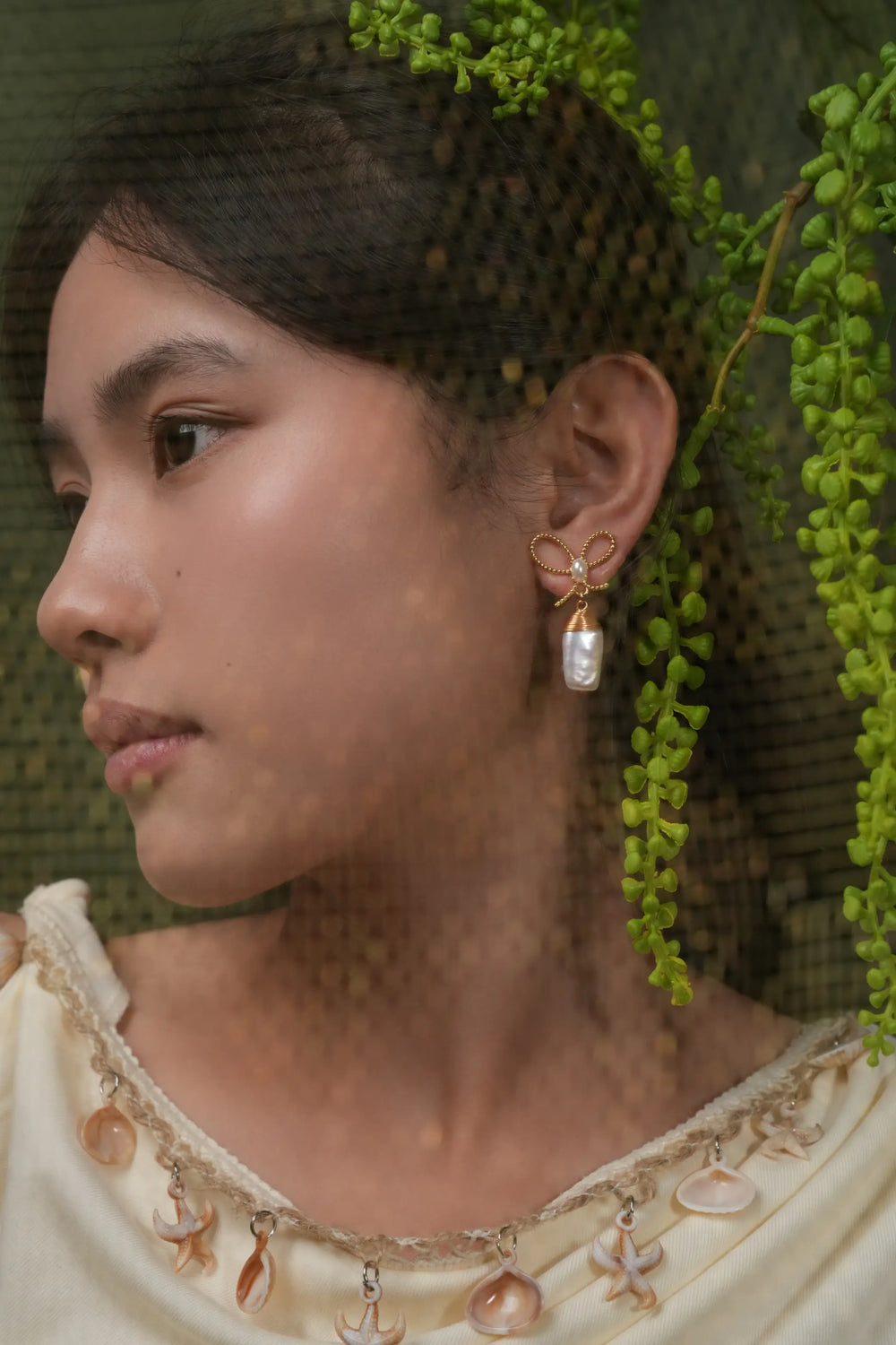 A woman wearing elegant gold ribbon pearl earrings.