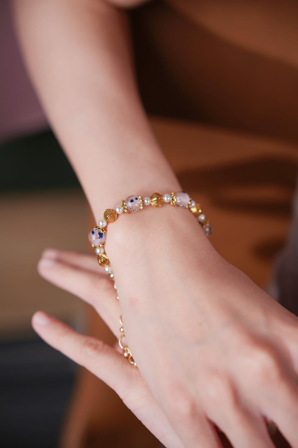 A hand wearing Elegant handmade beaded bracelat featuring light pink hand-blown glass beads with green, blue, and gold Eastern floral ink patternsGold bracelet.