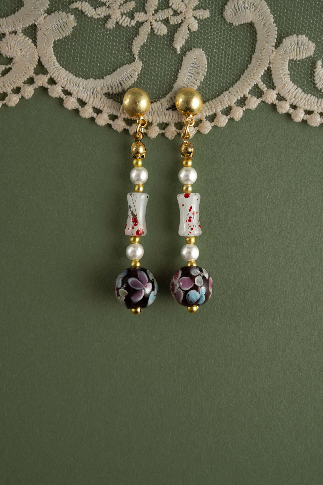 Handmade black floral glass bead dangle earrings with pearls, unique Asian-inspired blossom drop earrings for women, gold-plated boutique jewelry on green lace background